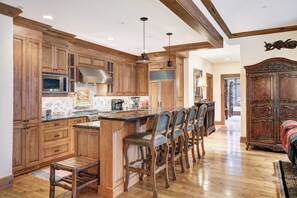 A spacious kitchen with wooden cabinets, a central island with bar stools, and a large wooden cabinet in the dining area. - NEW! 3BR Condo in Bachelor Gulch, Ski in/out (Avon)
