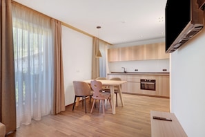 Een moderne keuken met houten kastjes, een eethoek met tafel en stoelen, en een aan de muur bevestigde televisie.