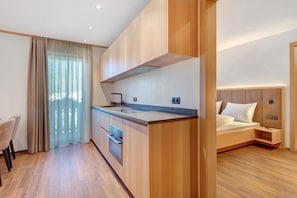 A modern hotel room with a kitchen area, a dining table, and a bed with a headboard. - Apartment 'Goldener Adler Premium 1' with Balcony and Breakfast Included  – new 2026 (Trodena nel Parco naturale)