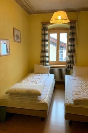 A room with two beds, a window with curtains, a radiator, and a hanging light fixture. - Chasa Stella, (Ftan) by Interhome (Ftan)