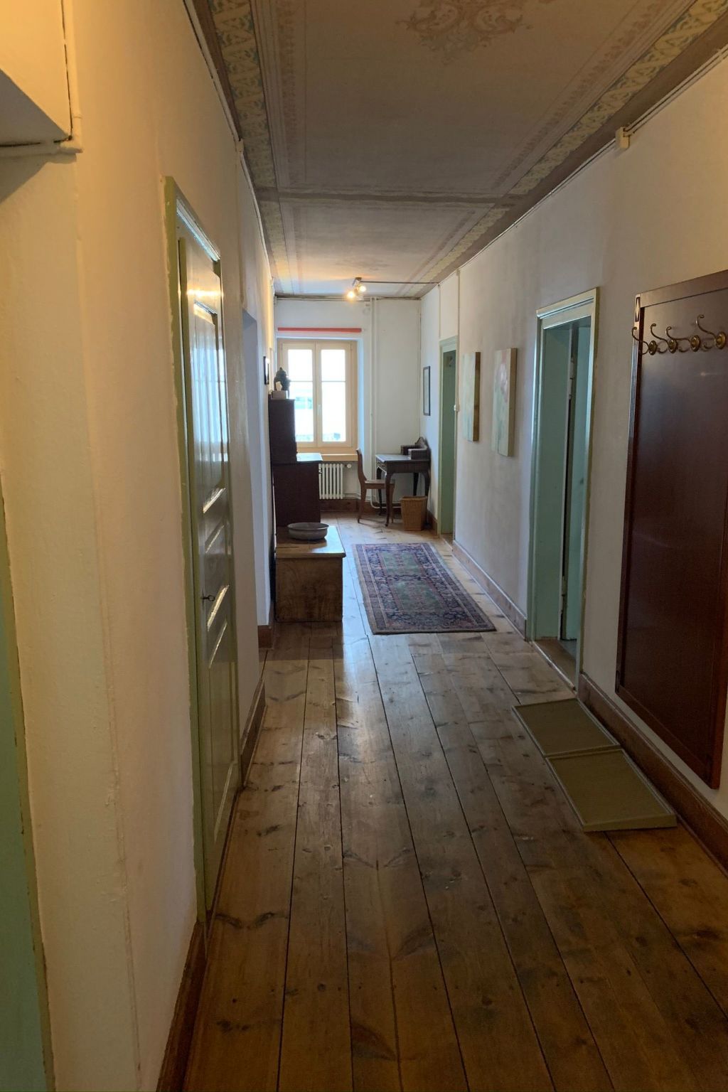 A hallway with wooden flooring, a radiator, a table with chairs, and a door with a decorative handle.