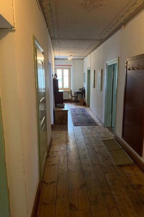 A hallway with wooden flooring, a radiator, a table with chairs, and a door with a decorative handle. - Chasa Stella, (Ftan) by Interhome (Ftan)
