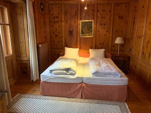A double bed with striped bedding, a bedside table with a lamp, and wooden paneling on the walls. - Chasa Stella, (Ftan) by Interhome (Ftan)
