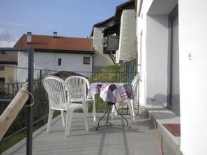Un balcon avec deux chaises blanches et une table recouverte d’une nappe à motifs.