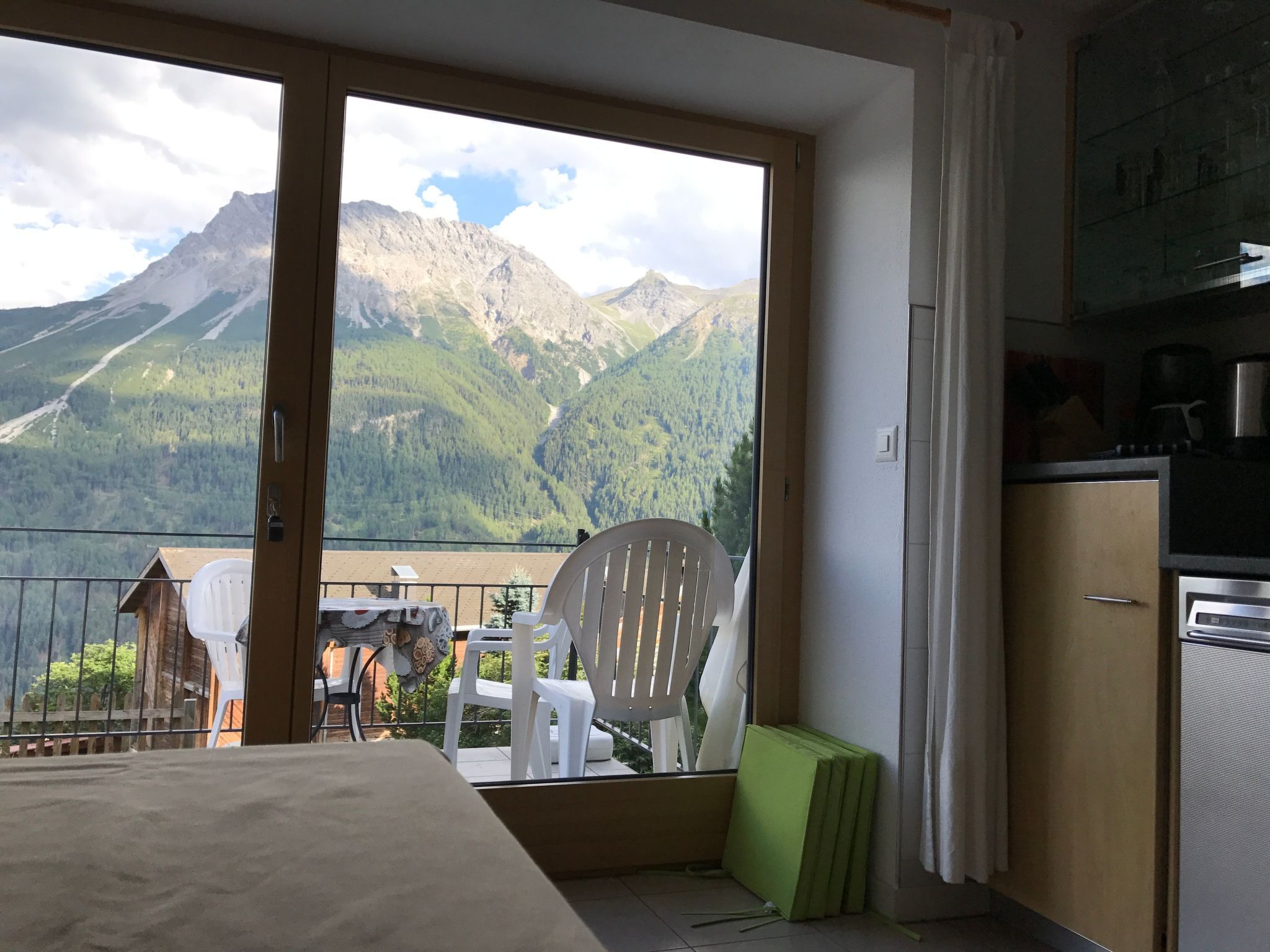 Een kamer met een groot raam, een eethoek met stoelen en een tafel, en een kitchenette.