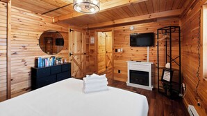 L’intérieur d’un chalet en bois comprend un lit, une commode, un miroir, une cheminée, un téléviseur et une étagère sur laquelle est posé un panneau.