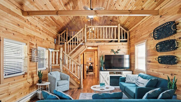 L’intérieur d’une cabane en bois comprend un espace de vie, un téléviseur, une cheminée et un escalier.