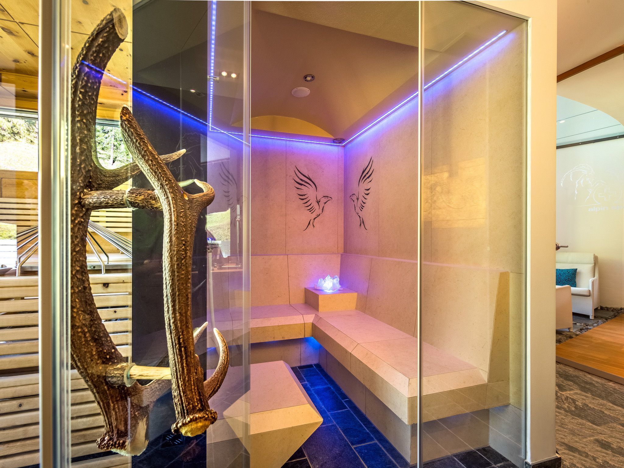 Un moderno spa con mampara de vidrio, una escultura de madera, un banco y una lámpara de pared.