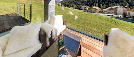 Een balkon met rieten meubels en een glazen tafel, met uitzicht op een berglandschap met een skilift.