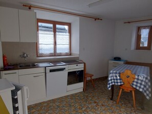 Cuina compacta amb finestra, un rentapeus, fogó i taula amb mantell a quadres.