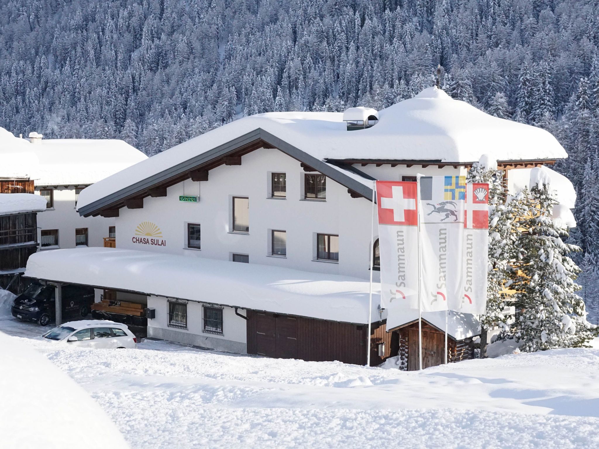 Un edificio cubierto de nieve con múltiples ventanas, un garaje y un letrero que dice 'CHASA SULAI'.