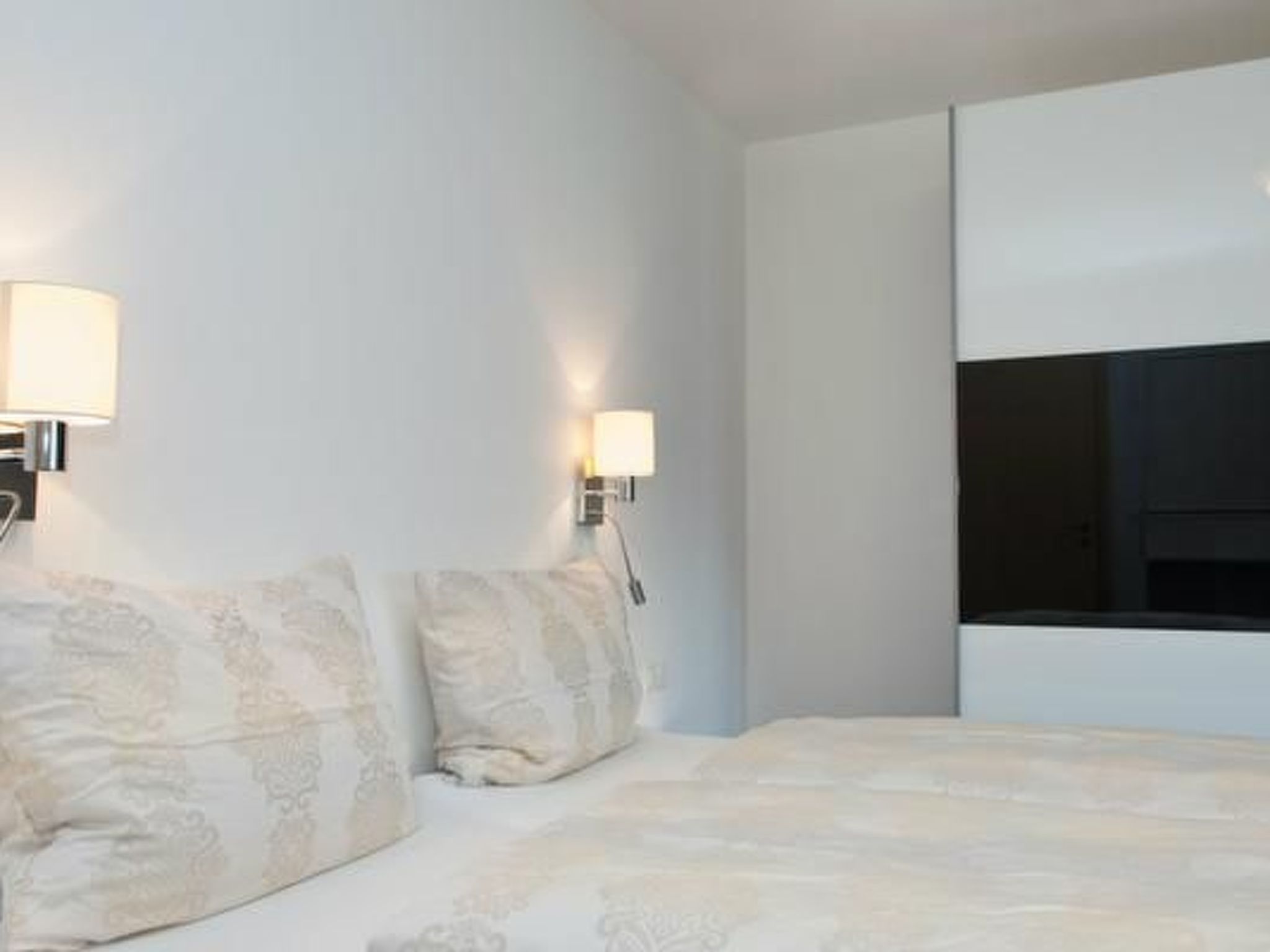 A hotel room with a bed, two wall-mounted lamps, and a large window.