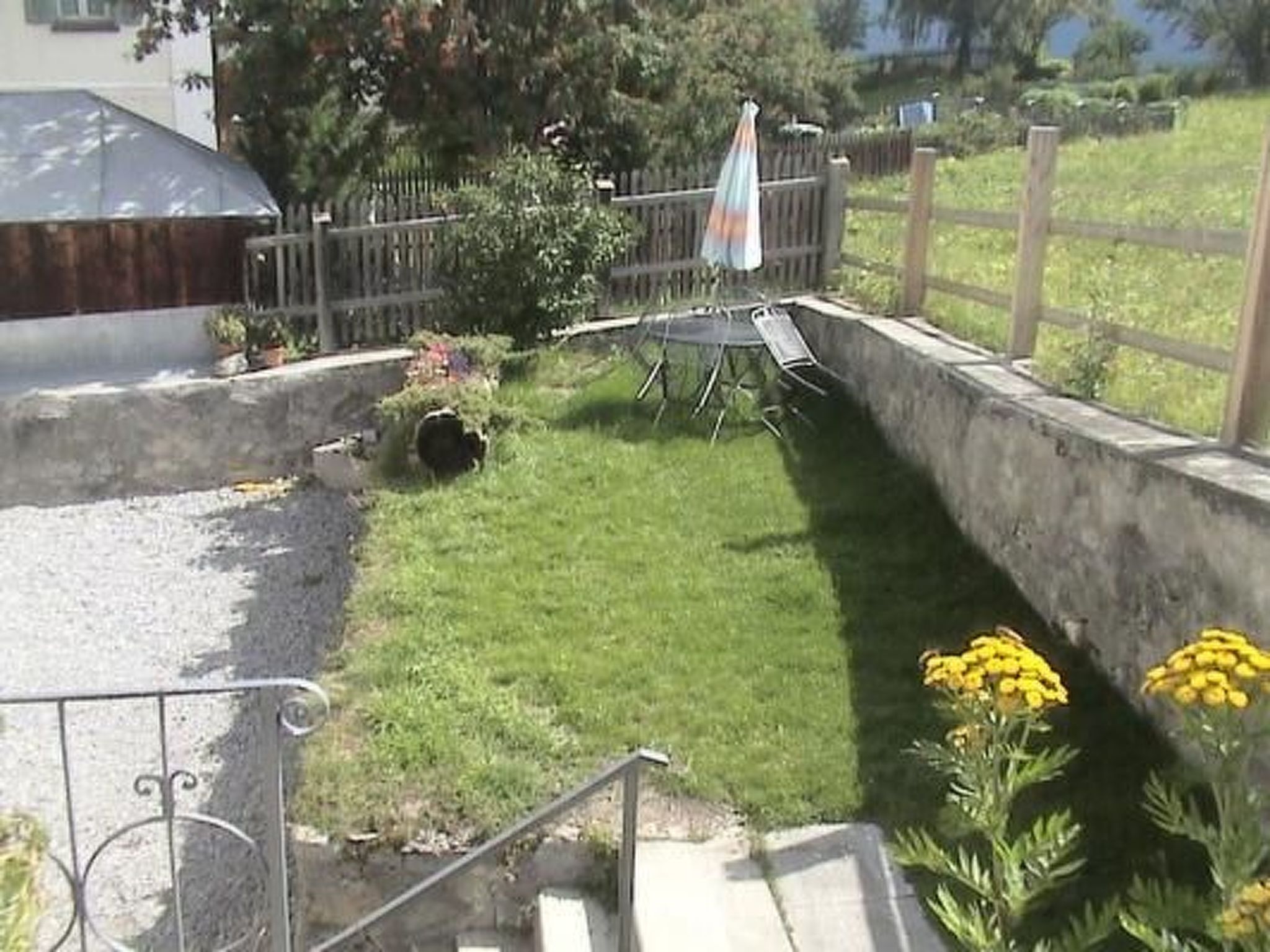 Un espacio exterior residencial con césped, un trampolín y un pequeño jardín con flores amarillas.
