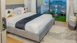 Een slaapkamer met een bed, uitzicht op de stad, een balkon met een tafel en stoelen, en een prullenbak.