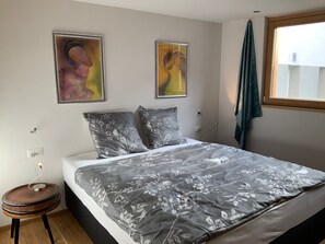 A bedroom with a bed, two pillows, a bedside table, a lamp, and two wall-mounted paintings. - Chasa Siringia EG, (Samnaun-Laret) by Interhome (Samnaun)