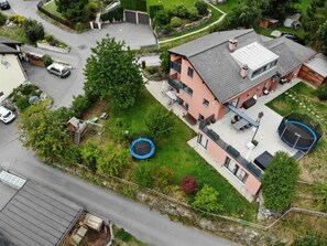 Una propiedad residencial con una casa de dos pisos, un patio trasero con un trampolín y un camino de acceso con automóviles estacionados.