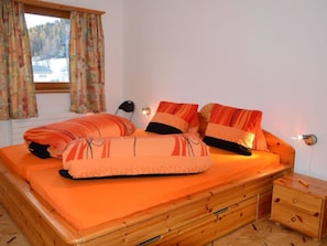 Une chambre à coucher avec un lit en bois, une literie orange, une table de chevet et une fenêtre avec des rideaux.