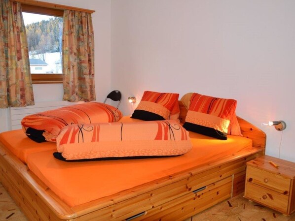 A bedroom with a wooden bed, orange bedding, a nightstand, and a window with curtains.