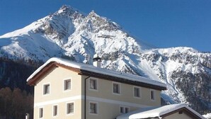 Um edifício de dois andares com telhado inclinado, várias janelas e uma montanha coberta de neve ao fundo.