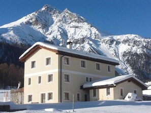 A two-story building with a sloped roof, multiple windows, and a snow-covered mountain in the background. - Villa Kuntner Bund, (Tschierv) by Interhome (Tschierv)