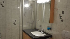 Casa de banho com chuveiro, pia e espelho.