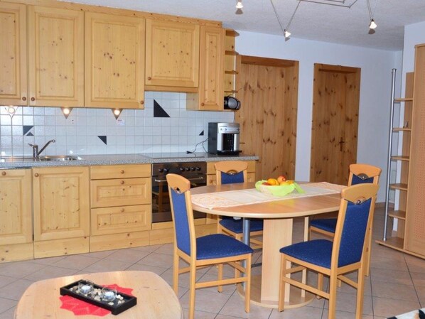 Una cocina con armarios de madera, una mesa de comedor con sillas y una cafetera.