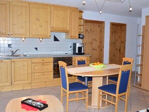 Une cuisine avec des meubles de rangement en bois, une table à manger avec des chaises et une machine à café.