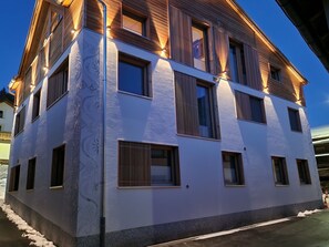 Un immeuble à plusieurs étages, doté d’une façade blanche et de détails en bois, avec de nombreuses fenêtres et une entrée bien visible.