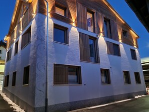 A multi-story building with a white facade, large windows, and wooden balconies.