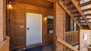 A wooden cabin with a white door marked '202,' a small porch with a doormat, and a wooden staircase. - Evergreen Escape by Velo (Angel Fire)