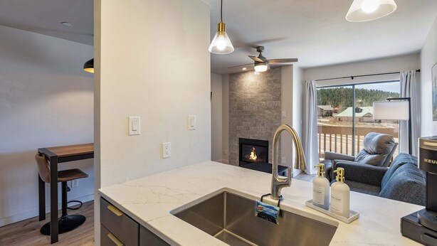 A modern kitchen with a large island, a built-in fireplace, and a view of the outdoors. - Evergreen Escape by Velo (Angel Fire)