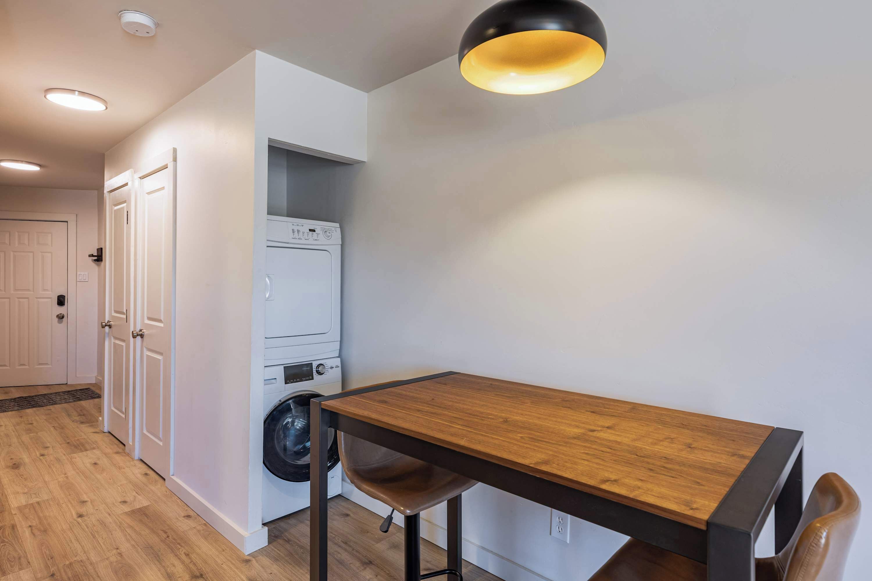 Cocina compacta con una mesa de madera, lavadora y lámpara en el techo.