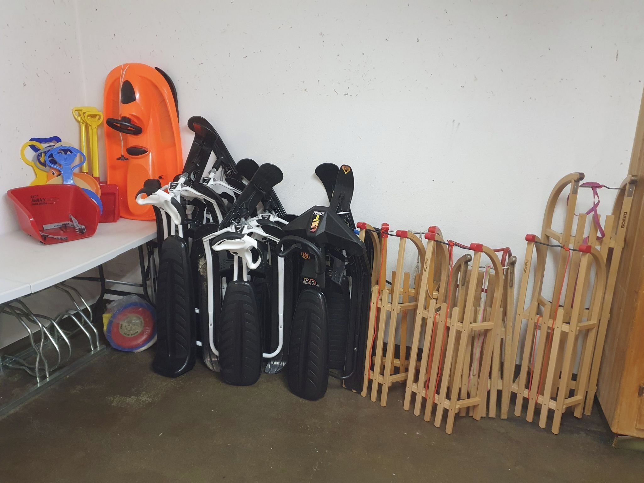 Un área de almacenamiento con diverso equipo, incluyendo cascos negros y naranja, un casco rojo, y sillas de madera.