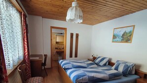 Une chambre à coucher avec un lit, un bureau, une chaise, une fenêtre avec des rideaux, un plafond en bois et un tableau accroché au mur.