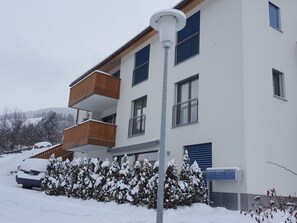 A multi-story residential building with balconies, a car parked in the driveway, and snow on the ground. - Chasa Scandella, (Sent) by Interhome (Sent)