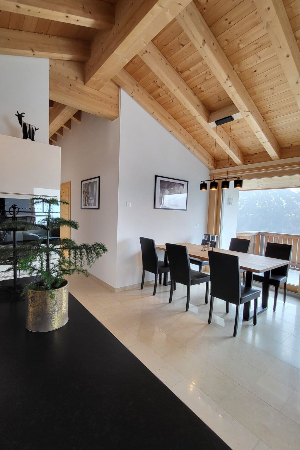 A modern interior with a dining area, wooden ceiling beams, and a potted plant.