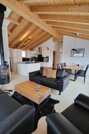 A modern interior with a wooden ceiling, a black leather sofa, a wooden coffee table, and a dining area with a table and chairs. - Chasa Scandella, (Sent) by Interhome (Sent)