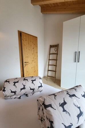 A bedroom with two beds, a wooden door, a ladder, and a wardrobe. - Chasa Scandella, (Sent) by Interhome (Sent)