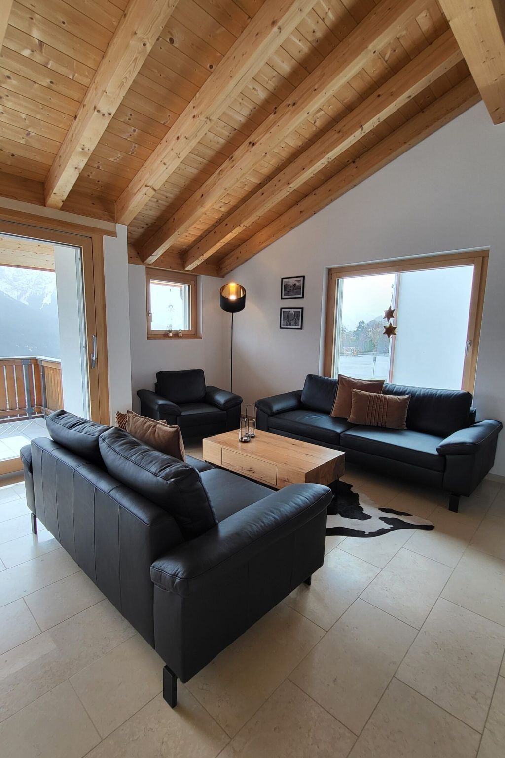 Een moderne woonkamer met een houten plafond, twee zwarte leren banken, een bijzettafeltje en een groot raam met uitzicht.