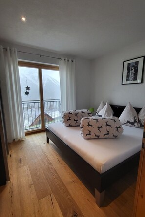 A bedroom with a bed, white curtains, a balcony with a view of snow-capped mountains, and a framed picture on the wall. - Chasa Scandella, (Sent) by Interhome (Sent)