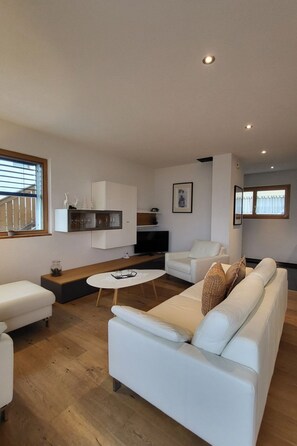 A modern living room with a white sofa, a coffee table, and a TV mounted on the wall. - Chasa Scandella, (Sent) by Interhome (Sent)