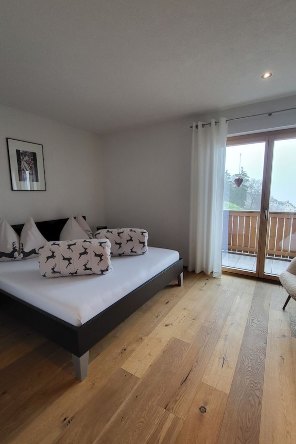 A bedroom with a bed, pillows, a picture on the wall, and a view through a glass door. - Chasa Scandella, (Sent) by Interhome (Sent)