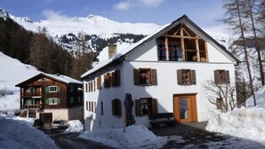 Un chalet de dos pisos con techo nevado, contraventanas de madera y balcón de madera.