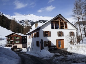 Un chalet à deux étages, avec un toit enneigé, des volets en bois et un balcon en bois.