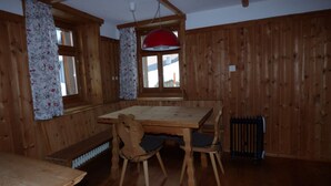 Una habitación con piso de madera, una mesa, sillas, un radiador y una ventana con cortinas.