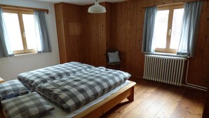 Una habitación con cama, una silla, paredes de madera y un radiador.