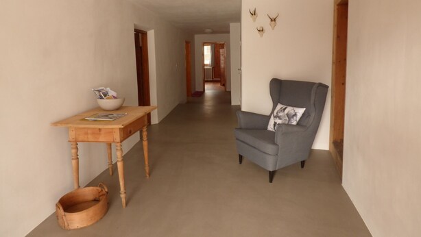 Un pasillo con una mesa de madera, un sillón gris y una decoración de cráneo de ciervo en la pared.