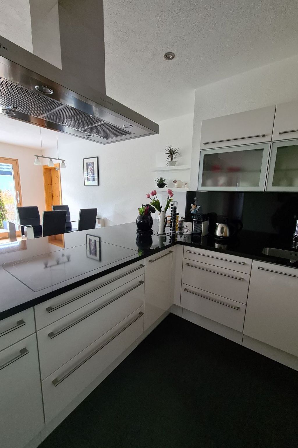 Een moderne keuken met witte kasten, een zwart aanrecht en een ingebouwde magnetron. Er is een raam met uitzicht op groen.