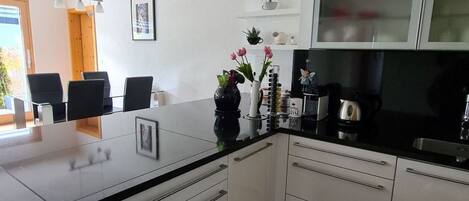 Een moderne keuken met witte kasten, een zwart aanrecht en een ingebouwde magnetron. Er is een raam met uitzicht op groen.