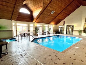 Ein Hallenbad mit Fliesenboden, Holzbalkendecke und mehreren Fenstern, durch die natürliches Licht einströmt.